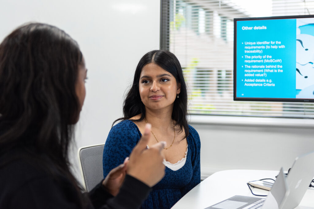 Two women talking beside a laptop in a classroom.