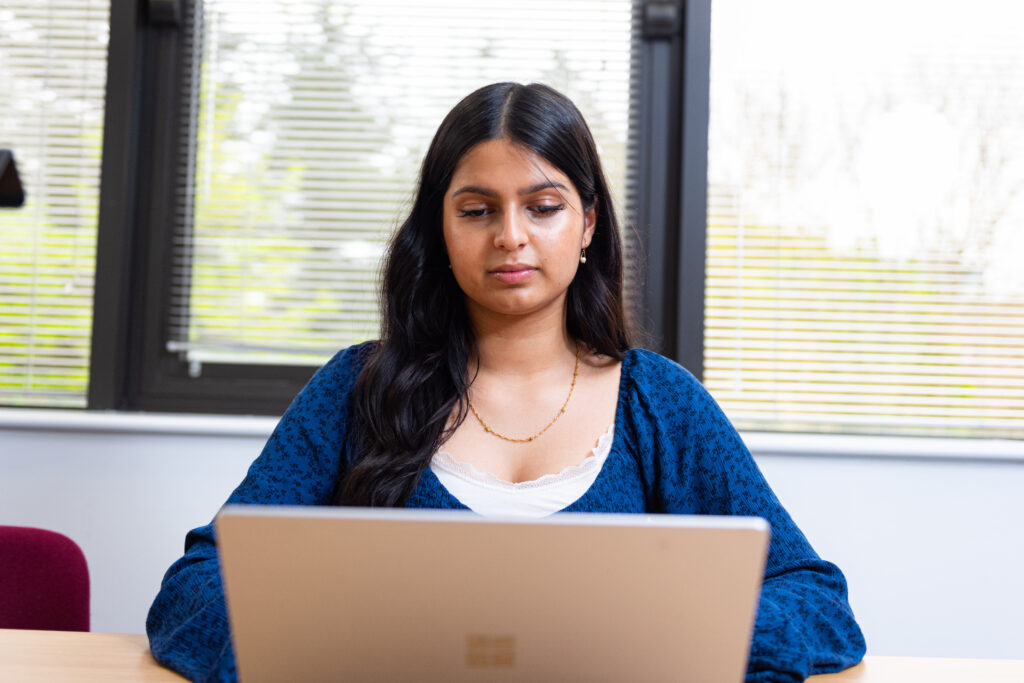 Woman working on a laptop beside a window.