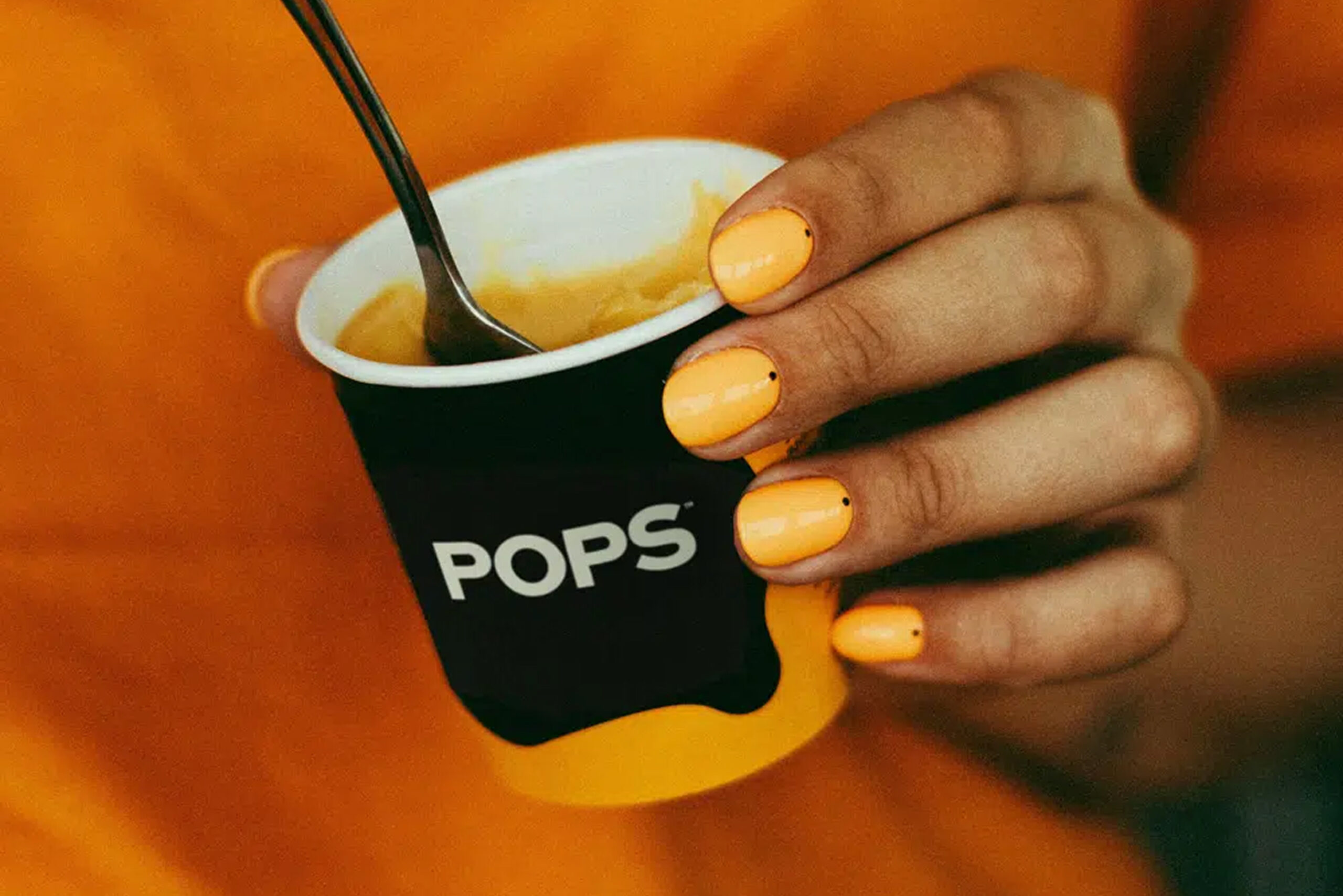 Hand holding a cup of POPS frozen cocktail with matching orange nail polish, highlighting vibrant branding.