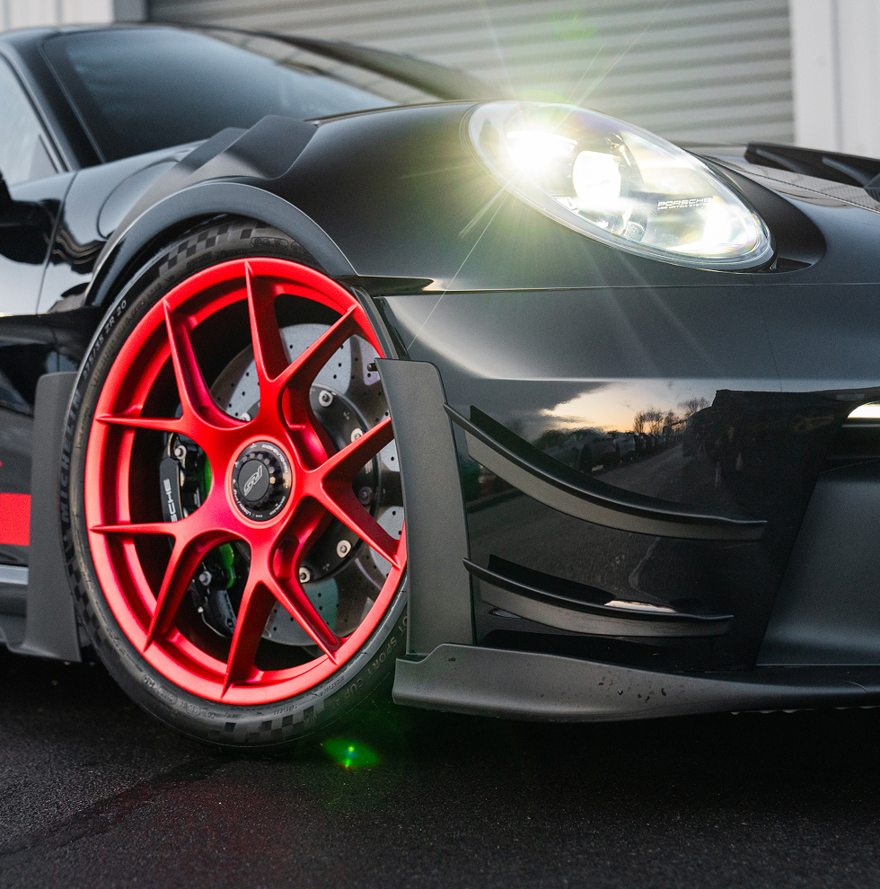 Close-up of a black Porsche sports car with red rims and glowing headlights.
