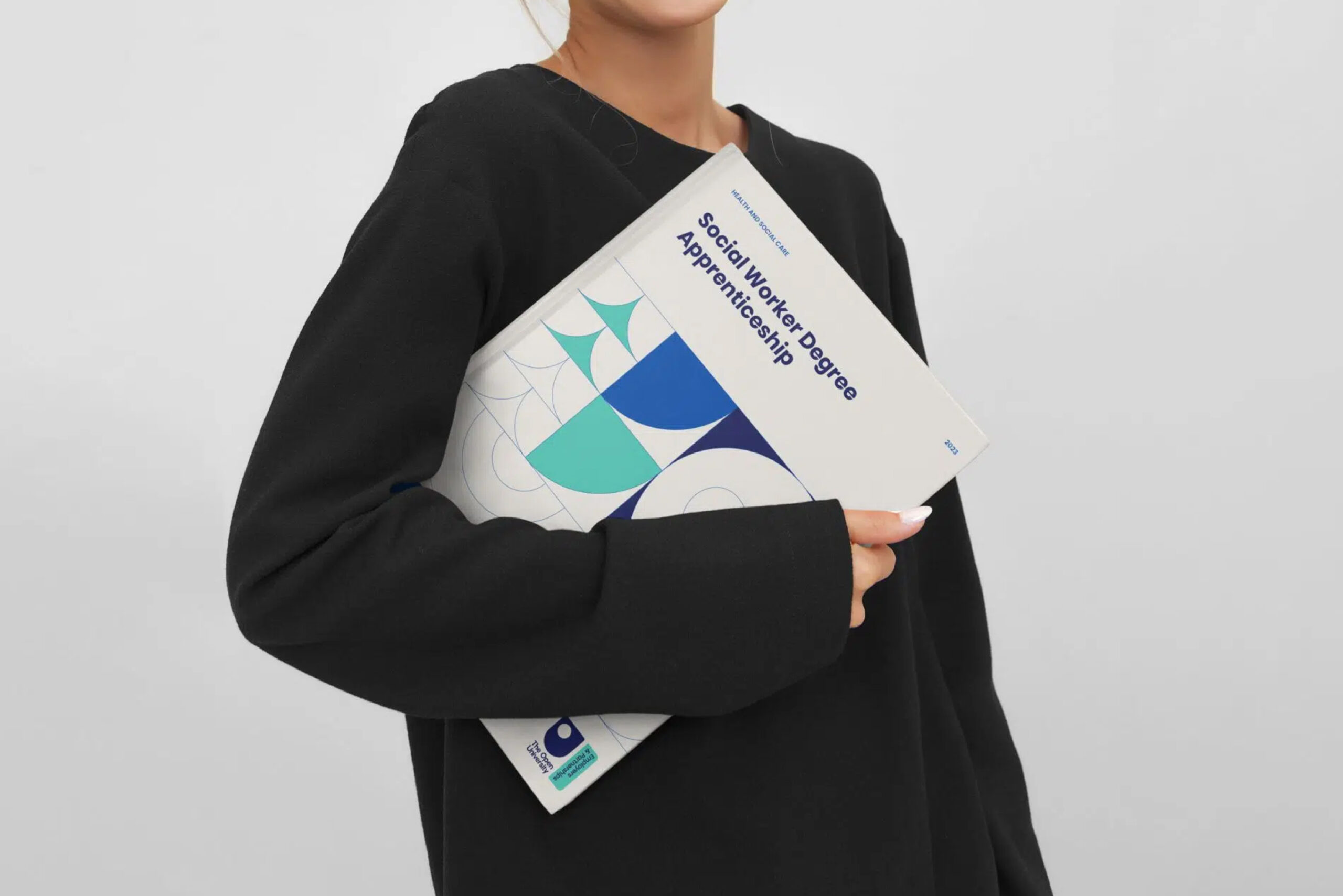 A person holding the "Social Worker Degree Apprenticeship" brochure from The Open University.