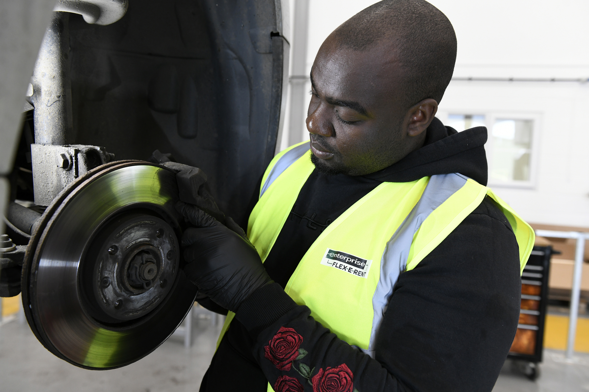 Mechanic examining the underside of a vehicle using a work light during maintenance at an Enterprise service facility.