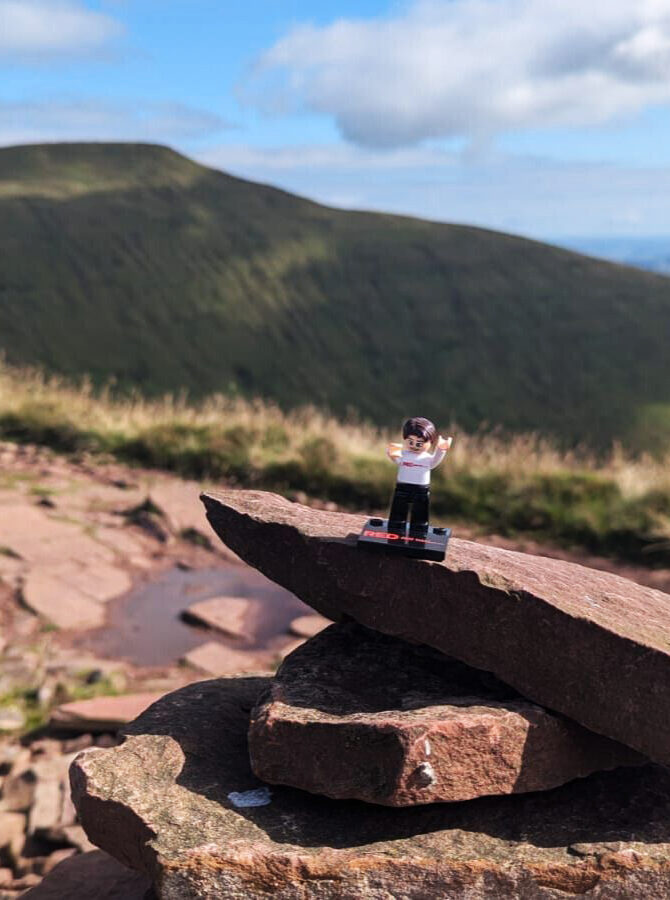 LEGO figure standing on rocks with mountains in the background.
