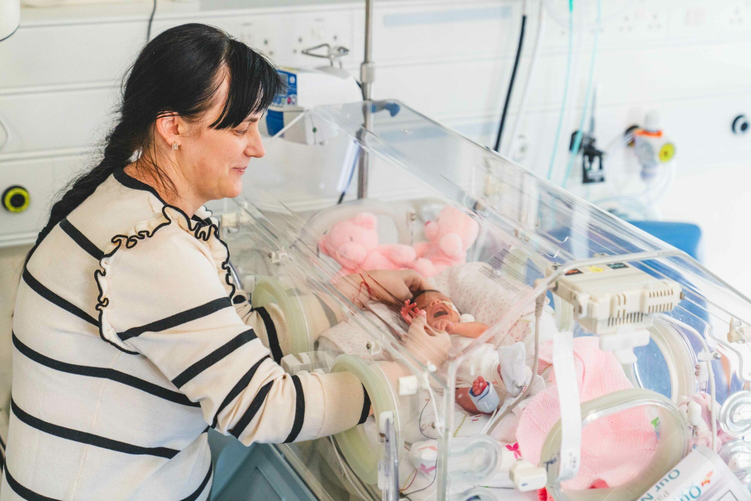 Mother comforting her newborn baby in a hospital incubator.
