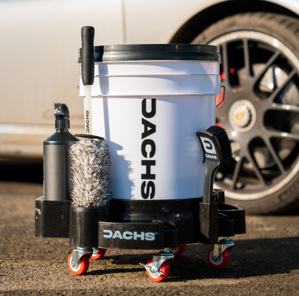 A Dachs branded car detailing bucket on a wheeled caddy, complete with cleaning brushes and supplies.