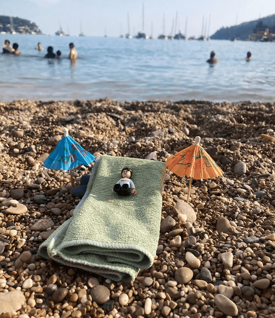 LEGO figure relaxing on a beach towel with umbrellas in the sand.
