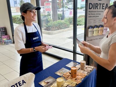 woman smiling and handing out a product sample